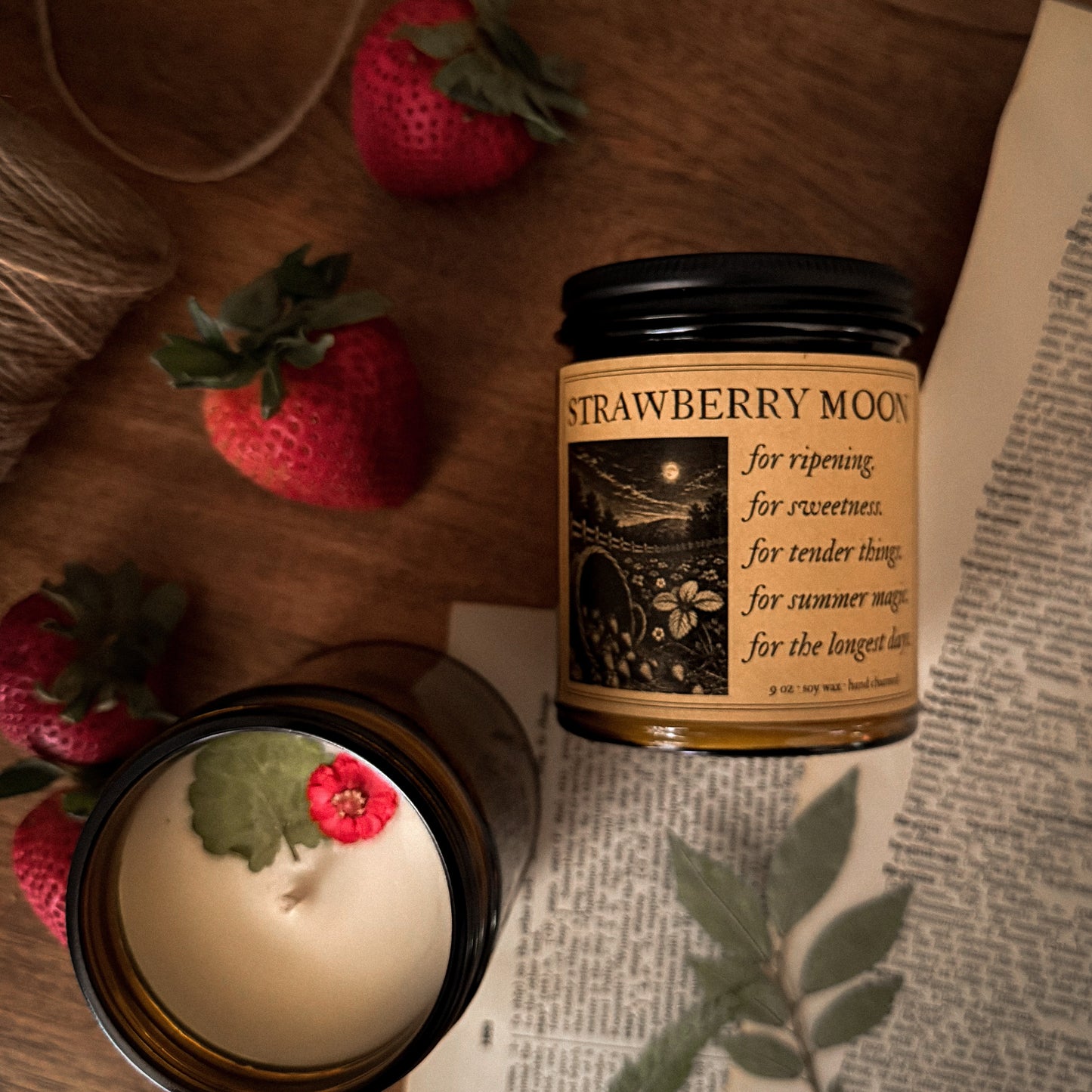 Jar of Strawberry Moon with strawberries and a candle on a wooden surface